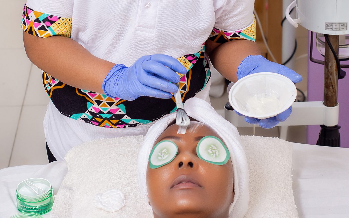Therapist applying a facial mask with cucumber slices on the eyes